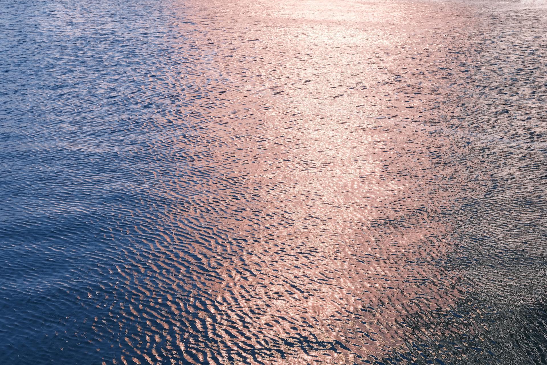 A calming view of sunlight reflecting off a rippling water surface, creating a textured pattern.