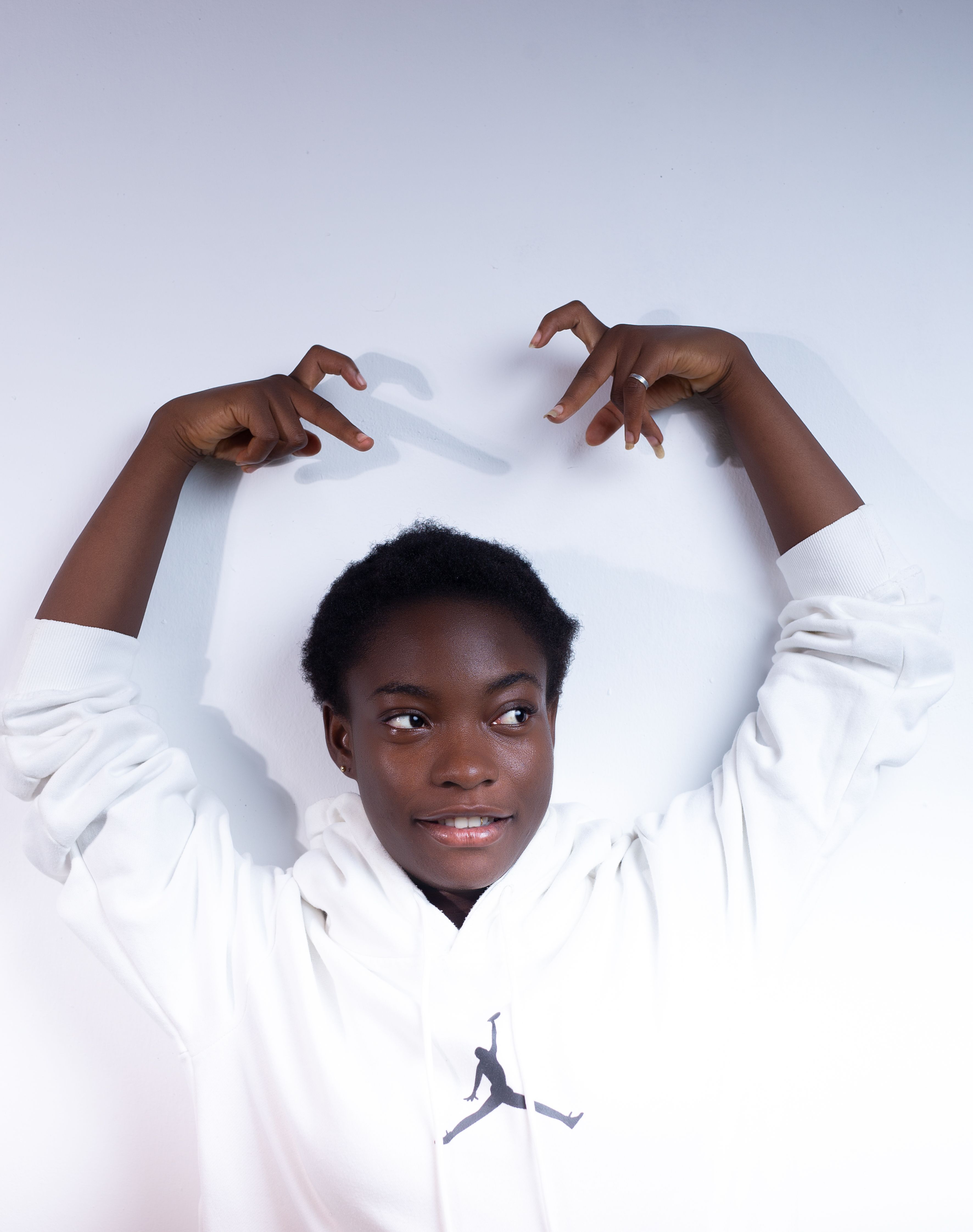 Teenager in a stylish white hoodie posing with raised hands against a minimalist background.