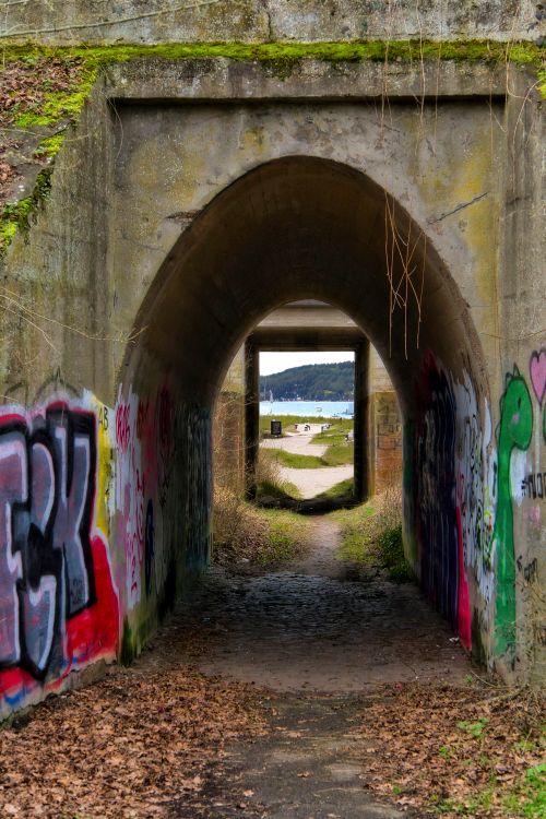 Free A graffiti-covered tunnel archway leading to a scenic outdoor landscape with a path and distant hills. Stock Photo