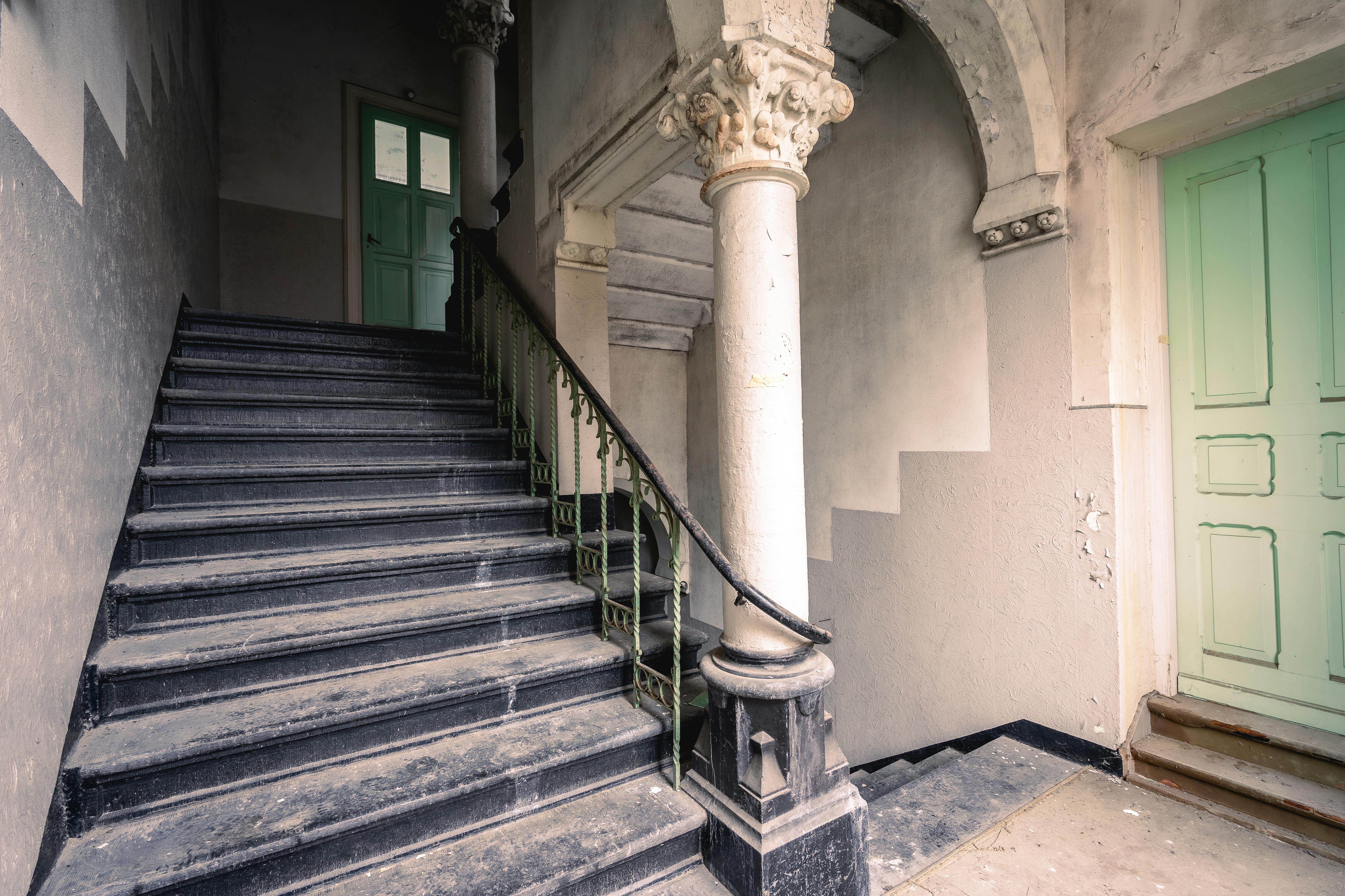 A forgotten staircase with ornate pillars in an abandoned building, exuding a gothic and atmospheric feel.