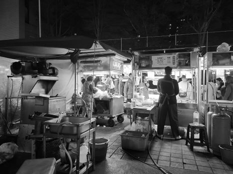 A bustling night market scene captured in black and white, showcasing food stalls and urban life at night.