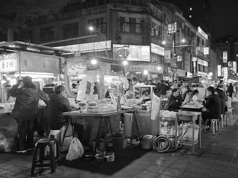Bustling night scene of an Asian street market with people enjoying street food and socializing.