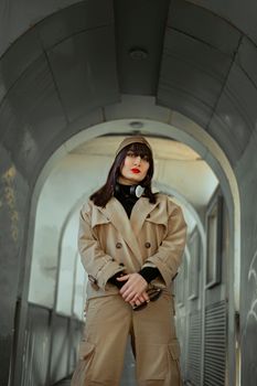 Fashion-forward woman posing confidently in a beige trench coat under a metal archway.
