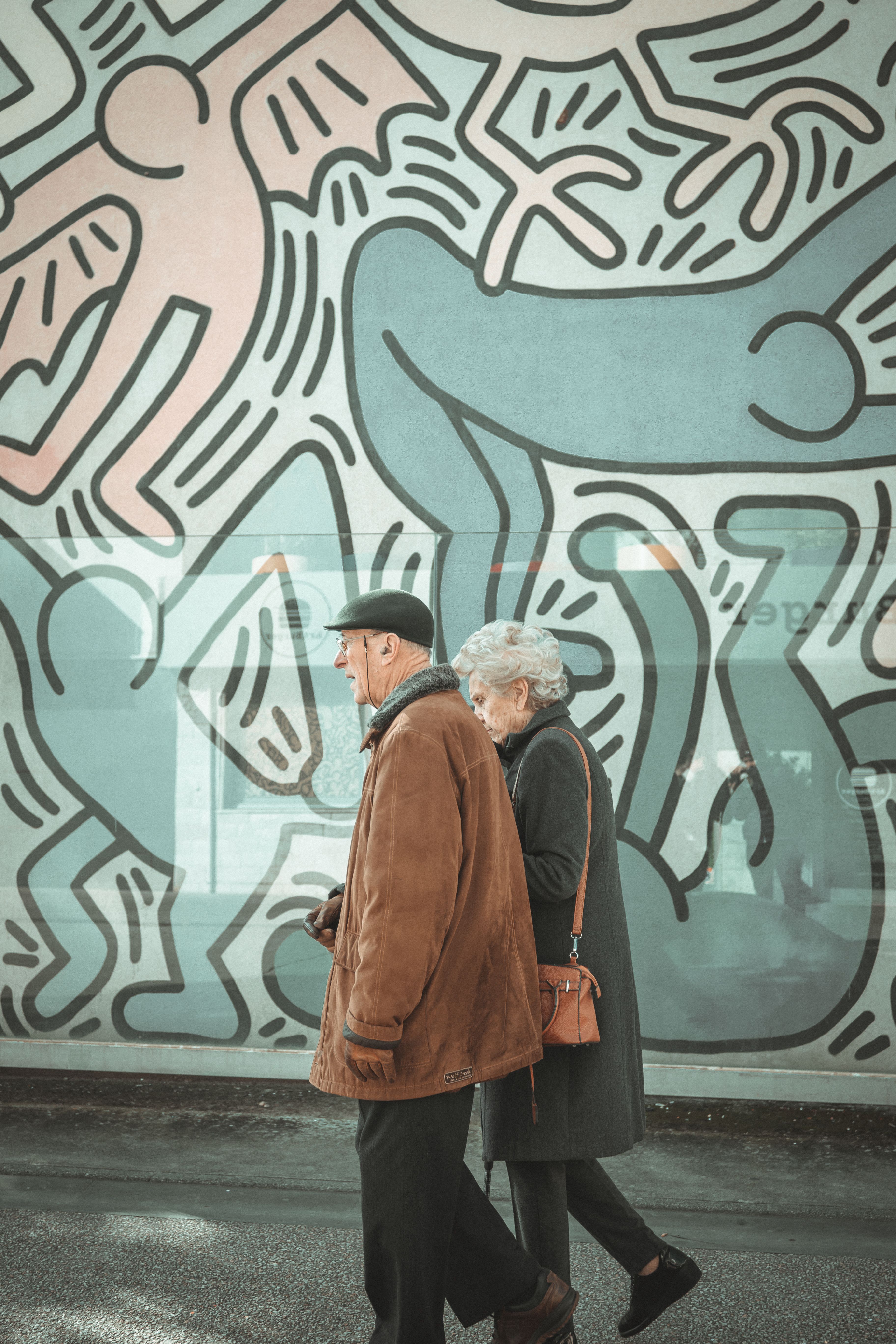 Senior couple strolls past a colorful urban mural, exploring street art in the city.