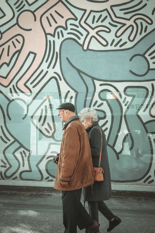 Free Senior couple strolls past a colorful urban mural, exploring street art in the city. Stock Photo
