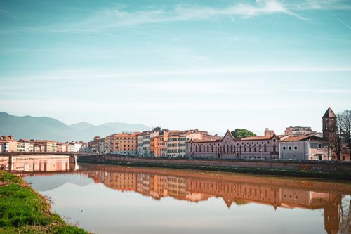 Free Panoramic cityscape of Pisa's riverfront with clear sky reflections. Stock Photo