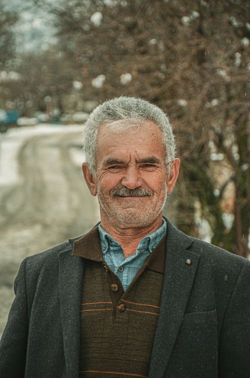 Free Portrait of a senior man in a coat smiling outdoors during winter with snow-covered trees. Stock Photo