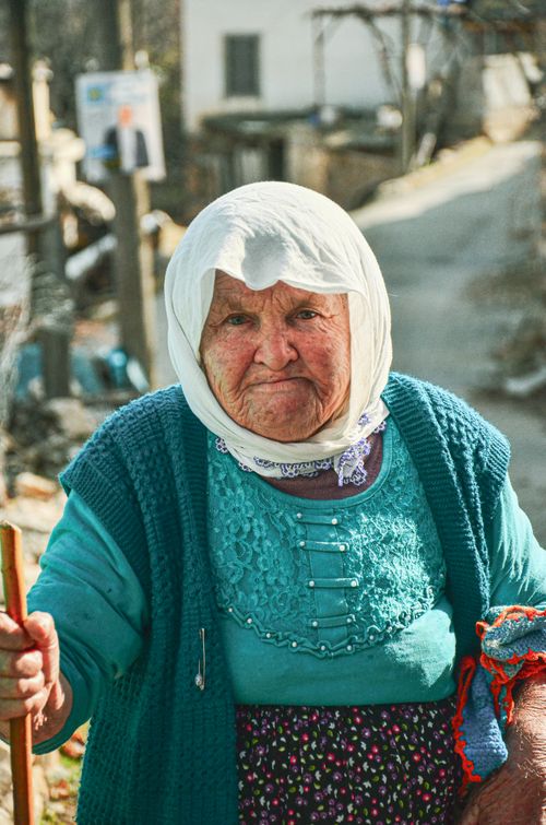 Free Portrait of an elderly woman wearing a headscarf, standing on a rural path, exuding warmth and tradition. Stock Photo