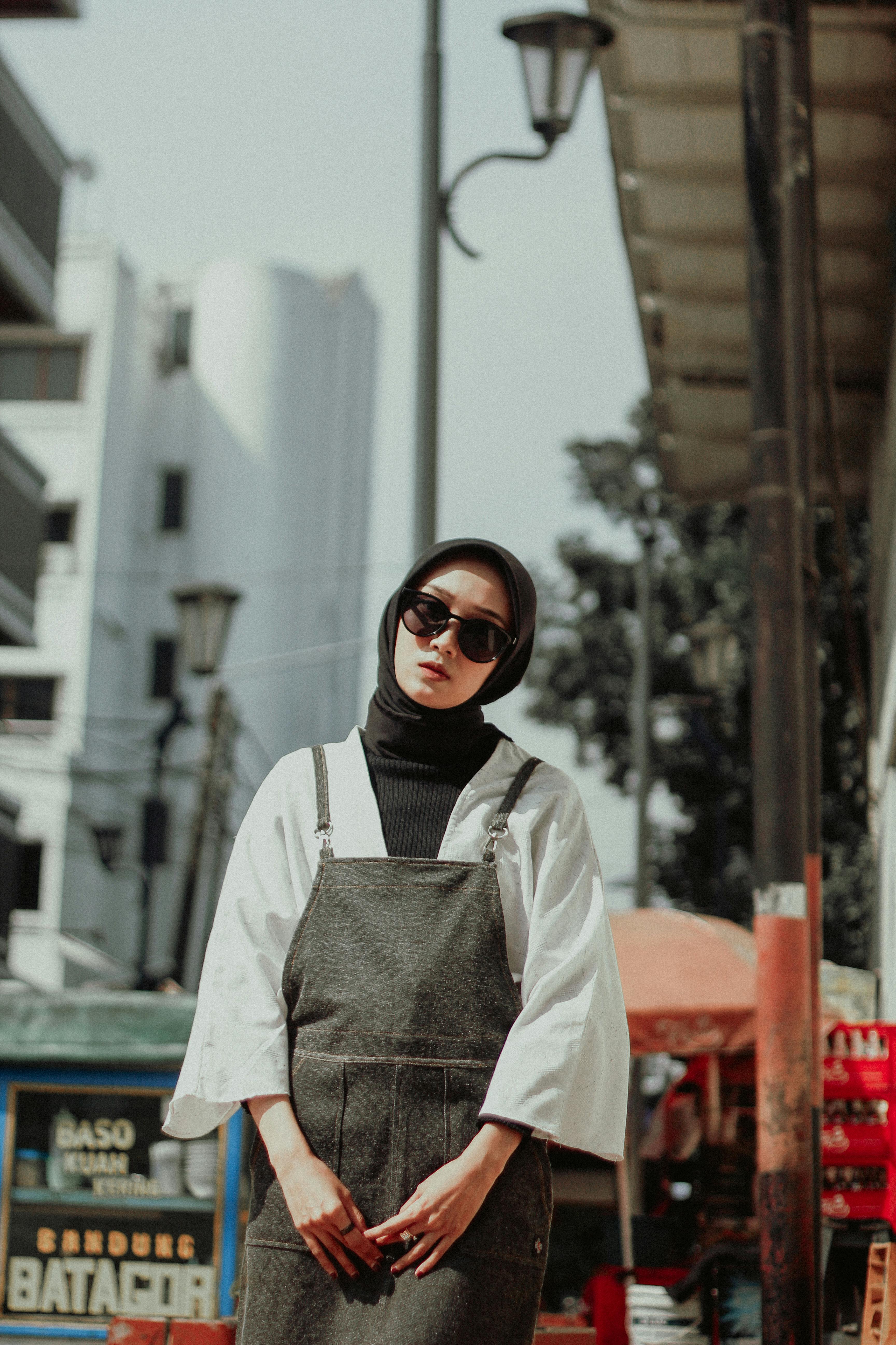 Sophisticated woman in hijab and sunglasses poses in trendy urban environment.