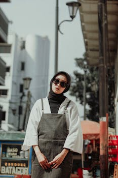 Sophisticated woman in hijab and sunglasses poses in trendy urban environment.