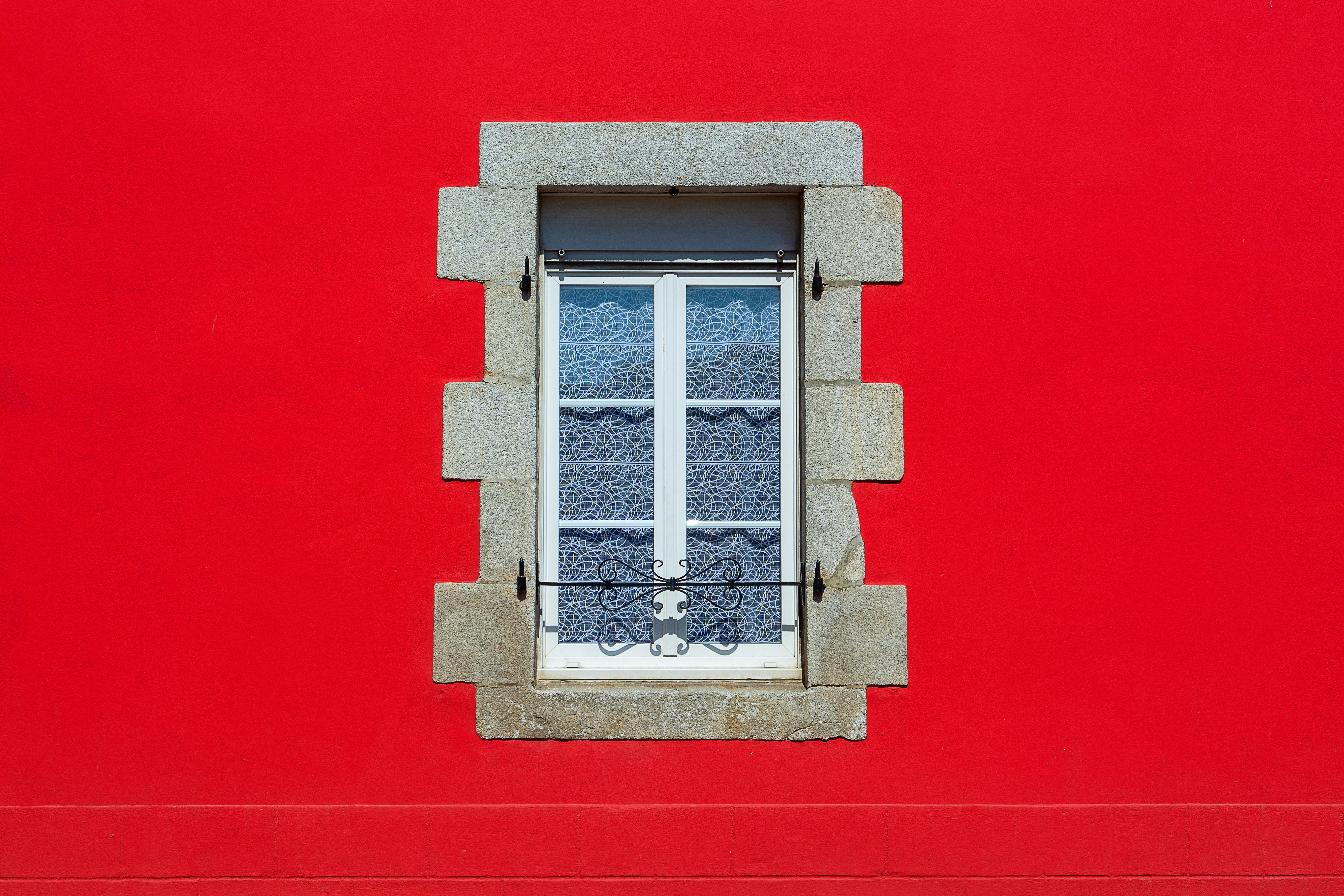 A charming white window set in a vibrant red wall with decorative lace curtains.