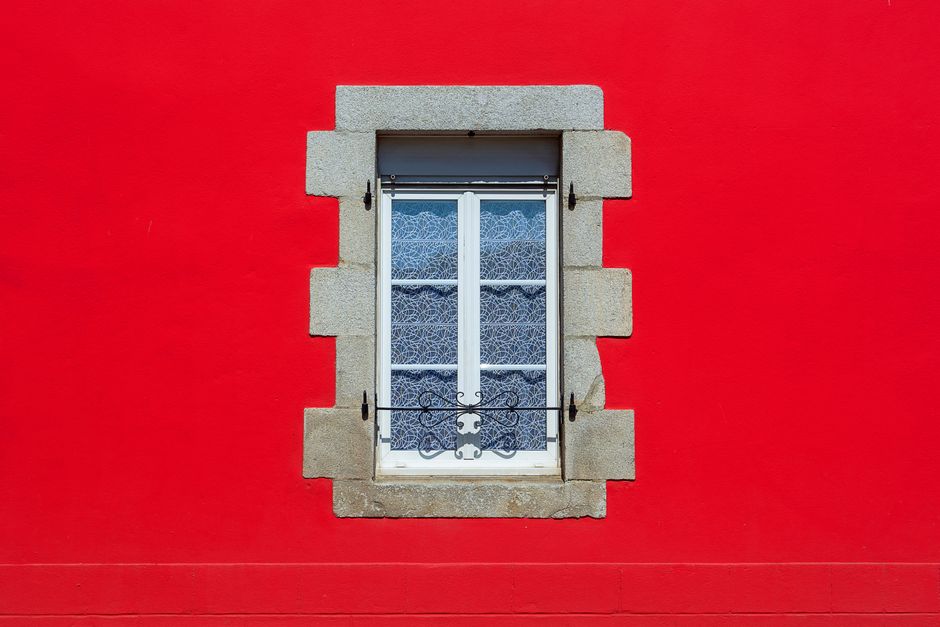 A charming white window set in a vibrant red wall with decorative lace curtains.