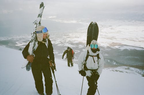 Two people carrying skis up a snowy mountain