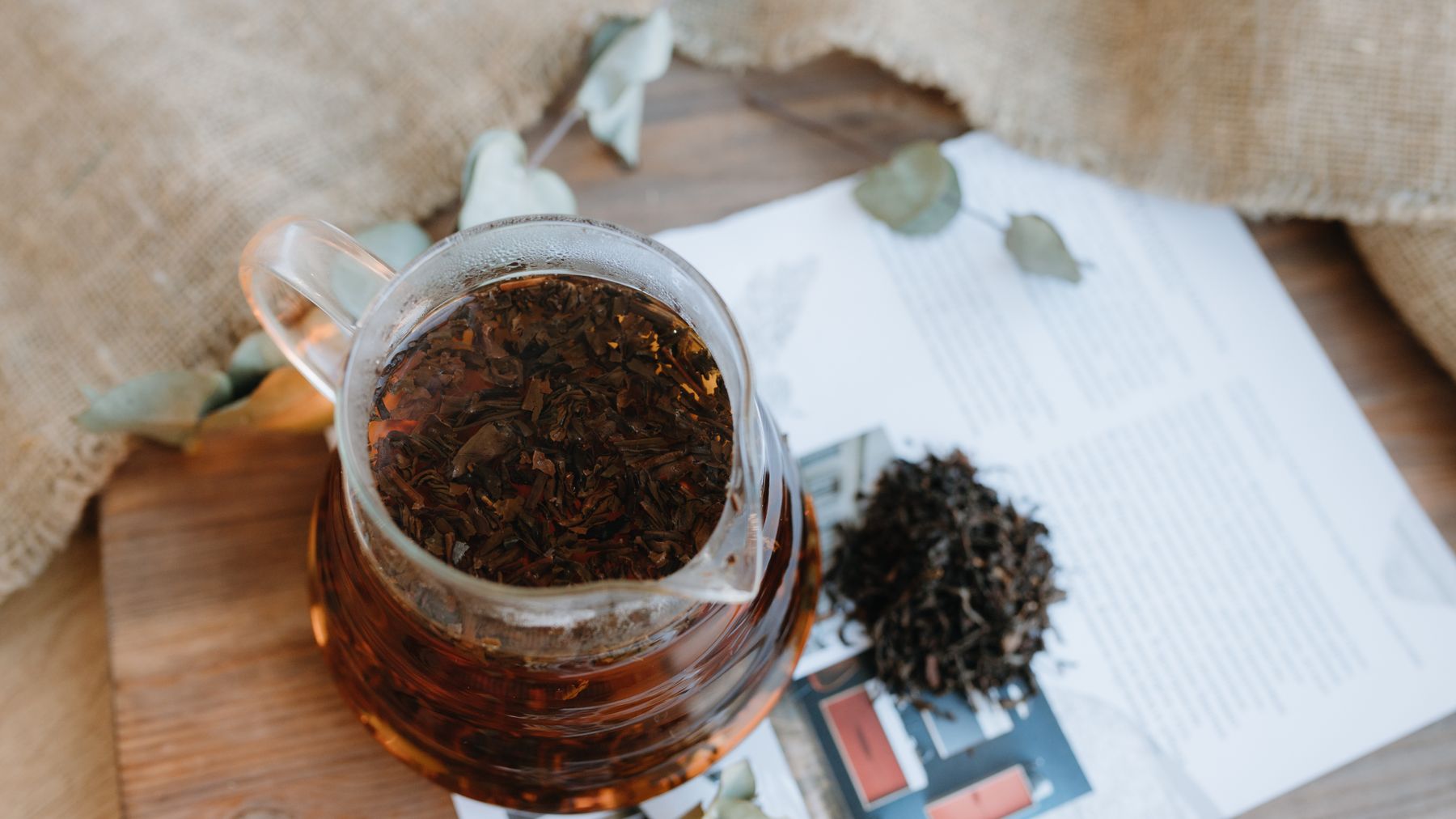 Overhead view of loose leaf tea in a glass pitcher, surrounded by rustic elements on a wooden table.