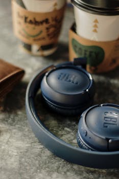 Dark blue wireless JBL headphones on a café table next to coffee cups, creating a cozy atmosphere.