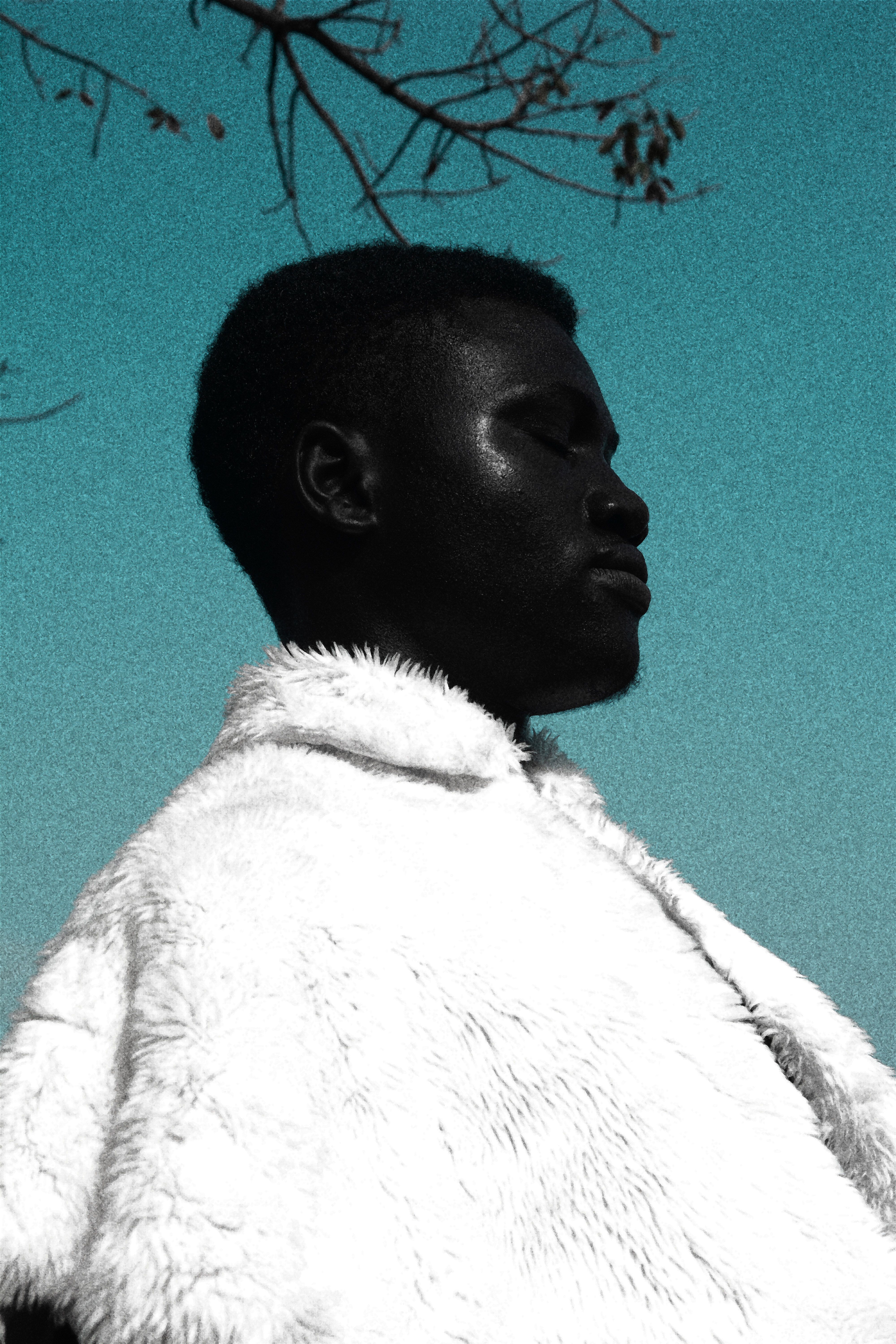 Artistic portrait of a man wearing a white fur coat against a sky backdrop in Lagos, Nigeria.