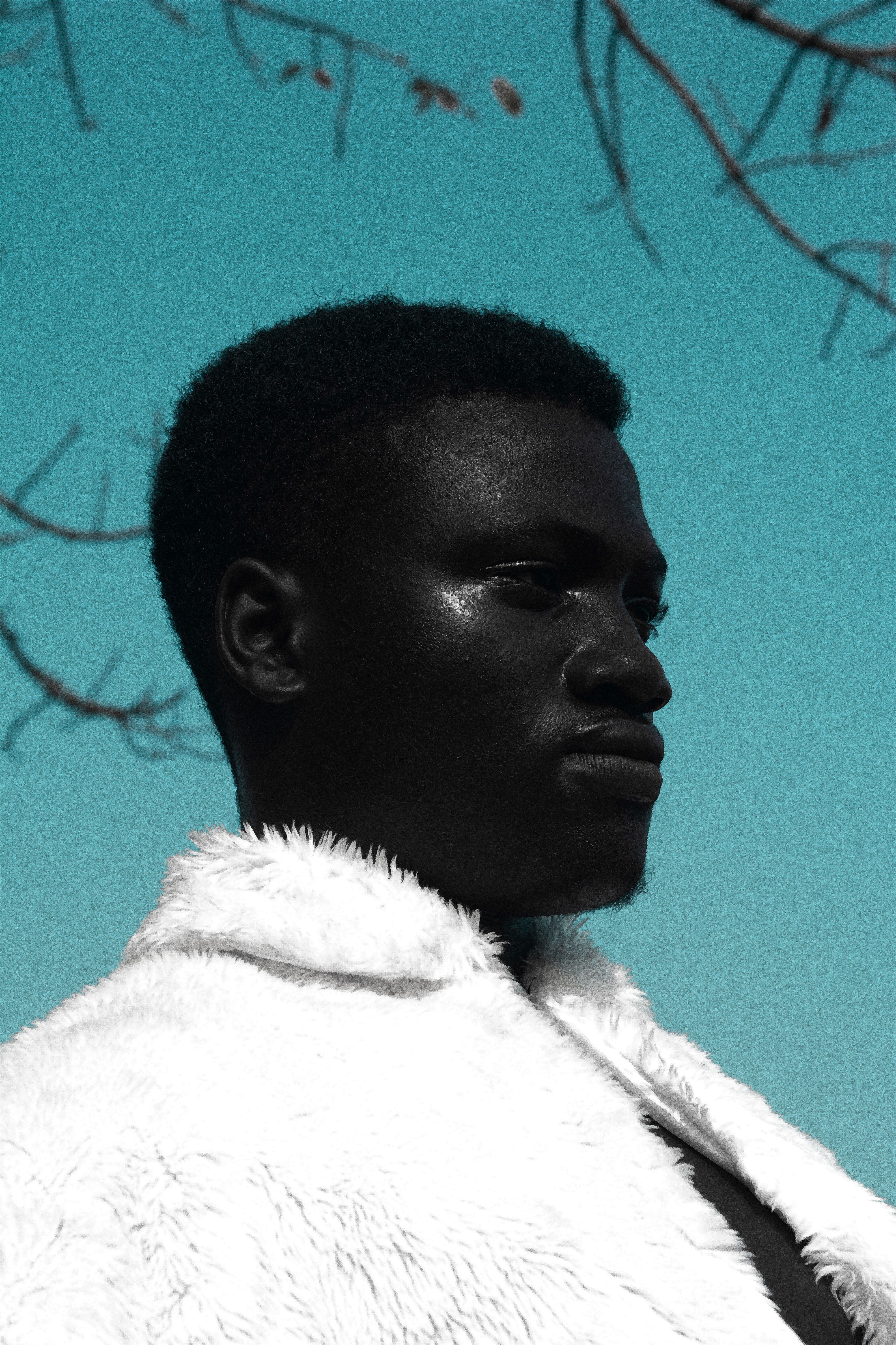 Artistic outdoor portrait of a black man wearing a white fur jacket against a blue sky.