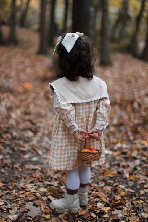 A little girl in a dress and hat walking through the woods