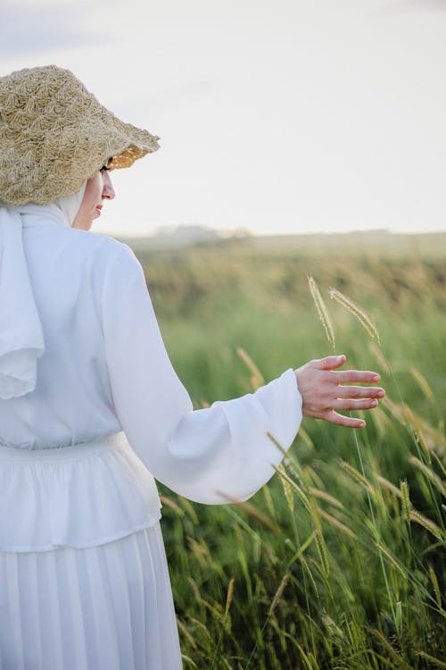 A woman in a white dress and hat is standing in a field