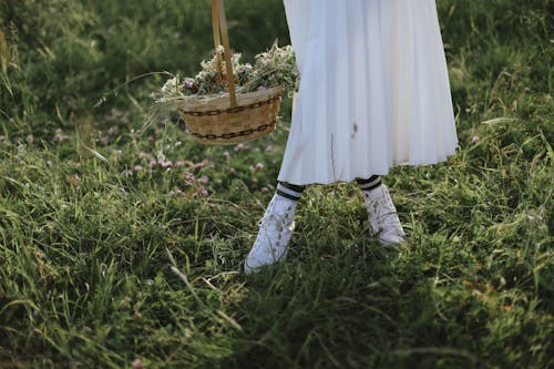 A woman in white dress and white shoes is holding a basket