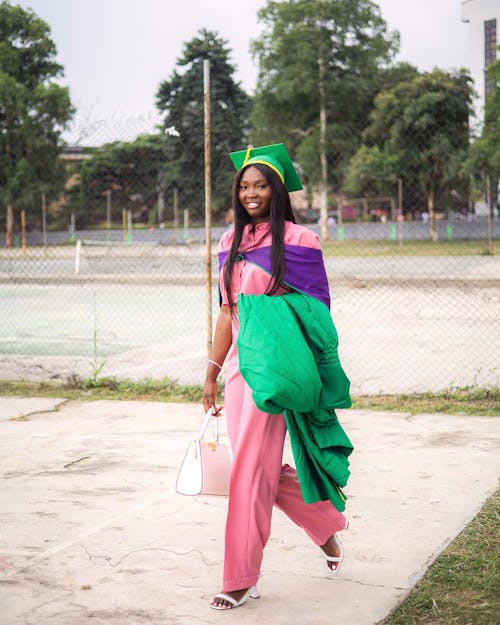 A woman in a pink and green graduation gown walking on the street