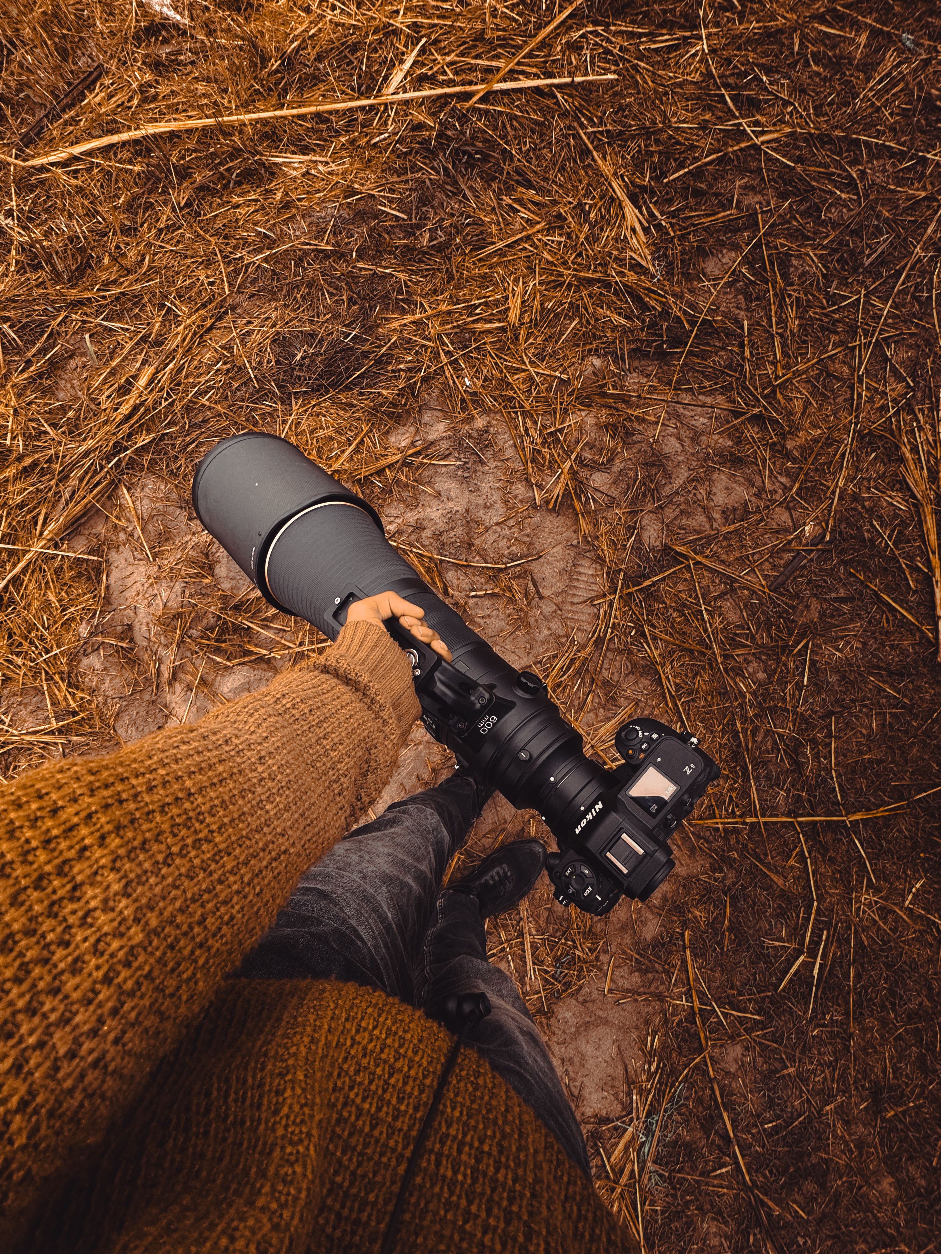 A person holding a large lens camera in an outdoor rural setting.