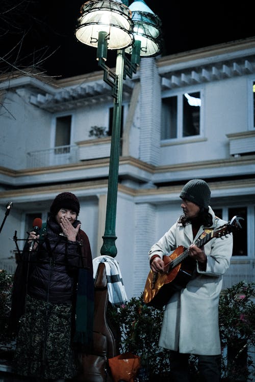 A man and woman playing guitar in front of a lamp post