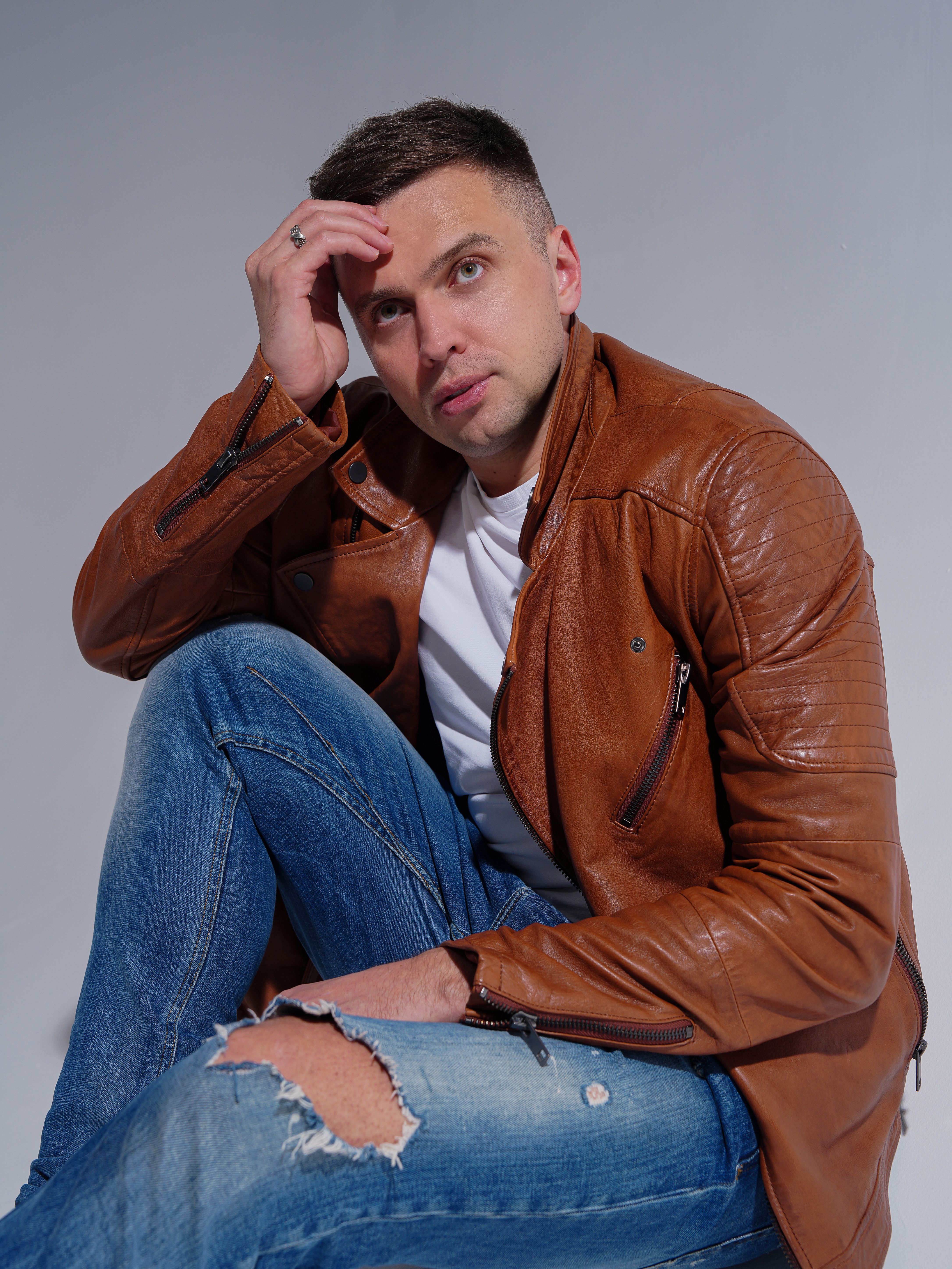 Studio portrait of a man in a leather jacket and jeans with thoughtful pose.