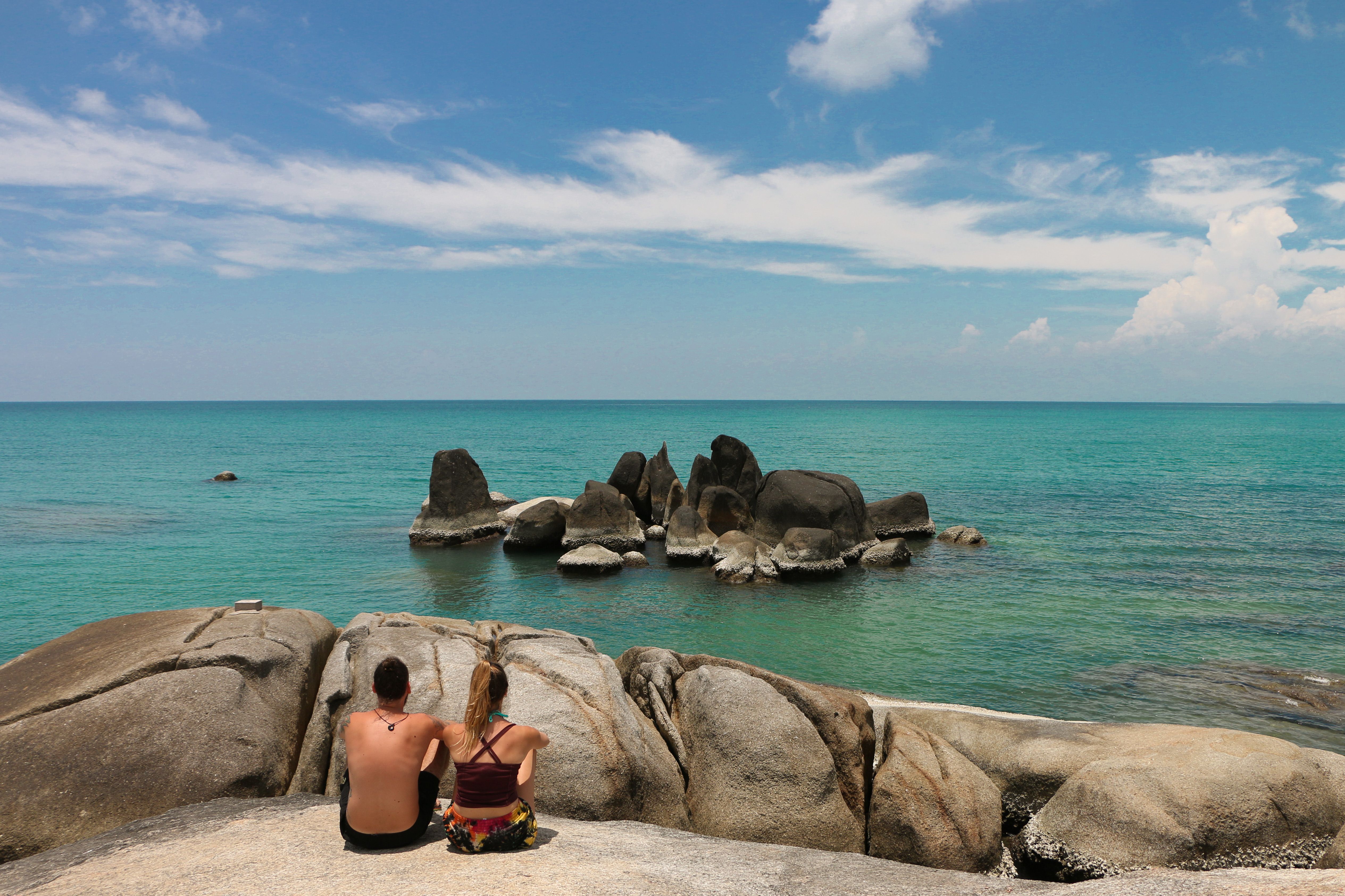 Couple Sitting near Rocks on Sea Shore in Summer · Free Stock Photo
