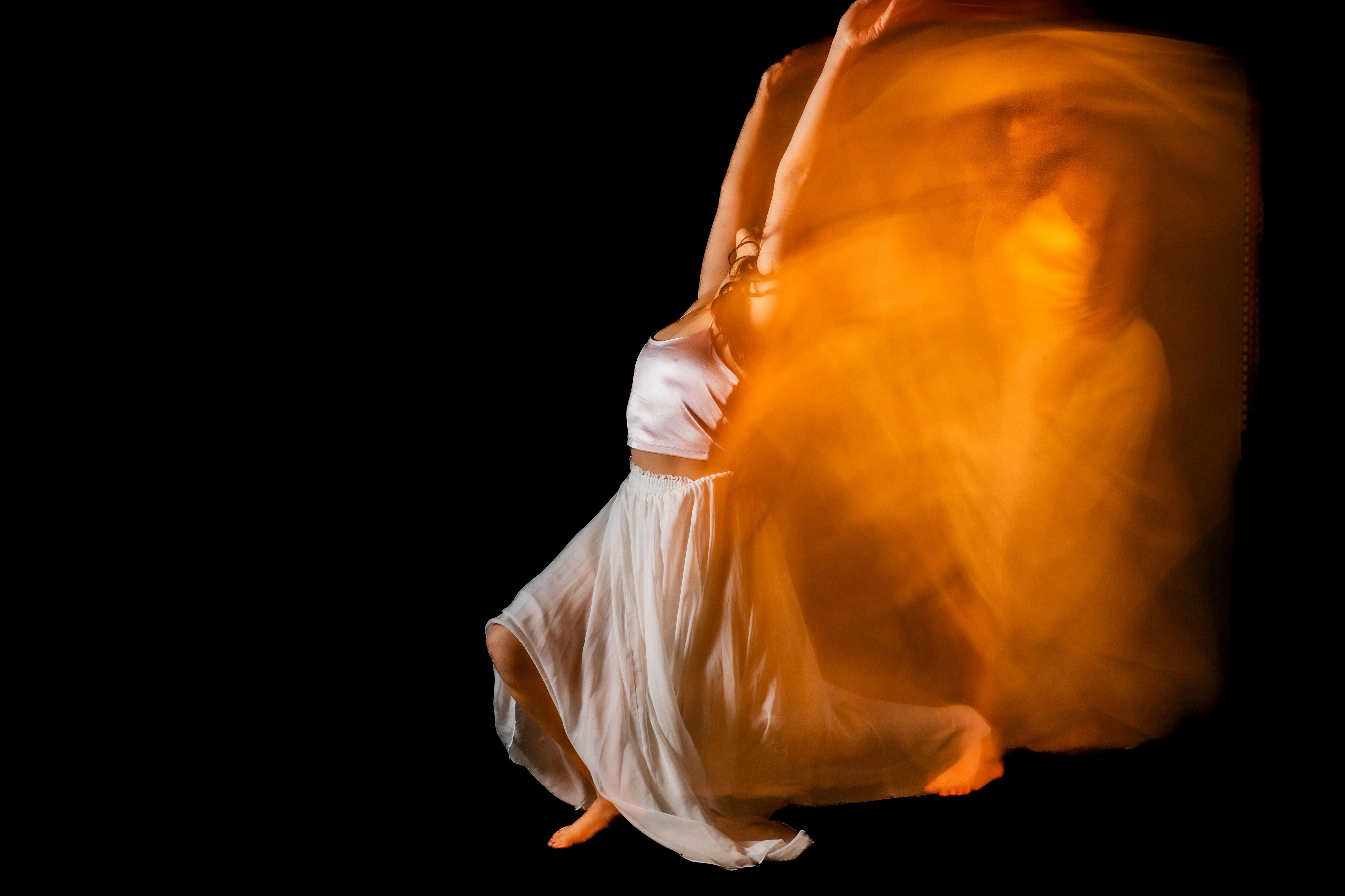 Artistic dance photo with motion blur effect, highlighting a woman in a white skirt against a black background.