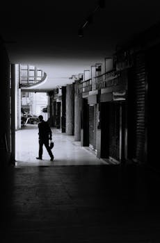 A man walks through a shadowy urban passageway, captured in black and white.
