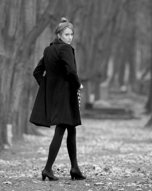 A woman in black coat and tights walking through a park
