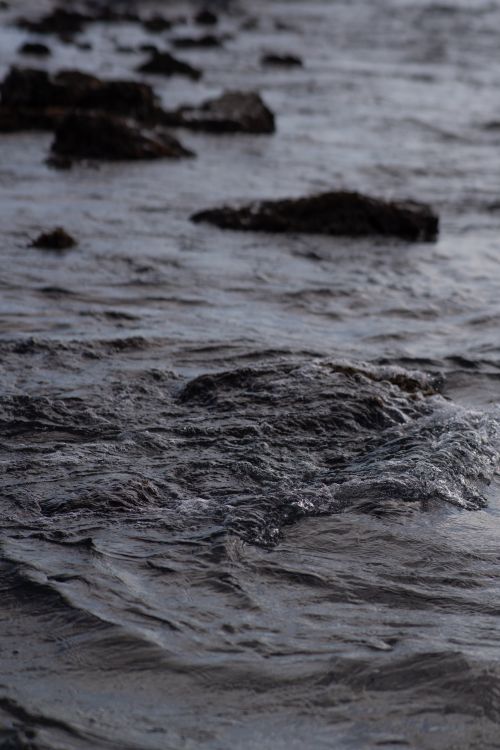 Free Gentle waves splashing over rocky terrain on a calm coast, captured in natural light. Stock Photo