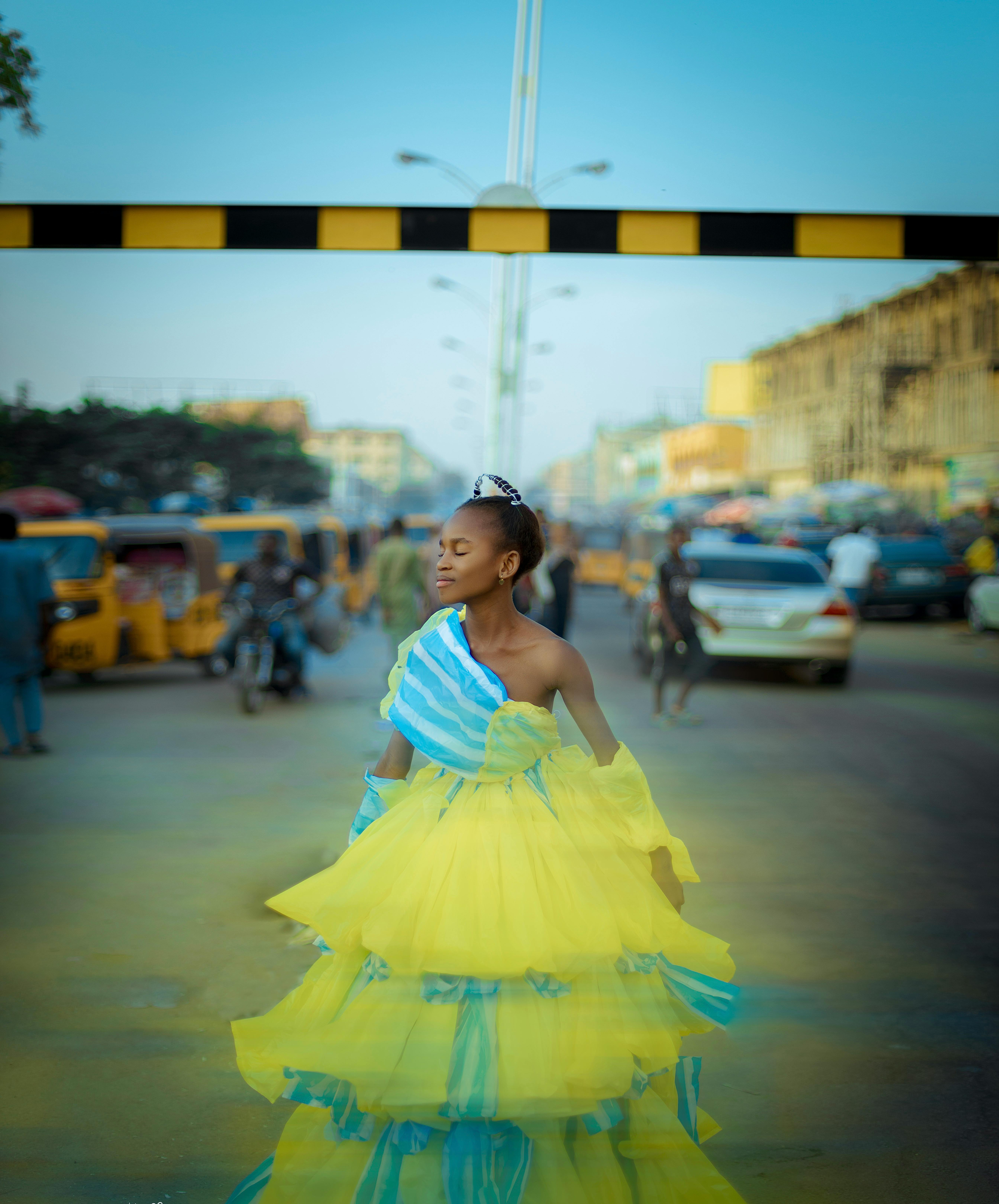 Woman in yellow and blue ruffled dress standing confidently on a bustling city street.
