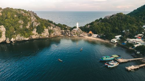 Free Drone shot of a scenic coastal harbor with lush greenery and vibrant boats. Stock Photo