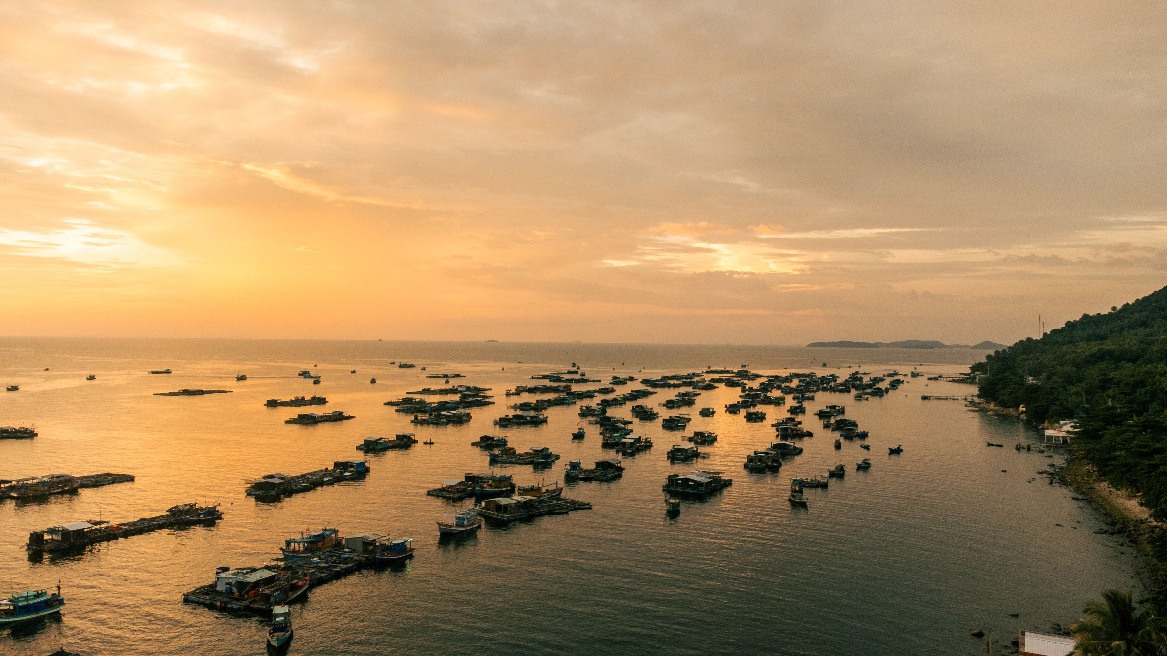 Serene aerial view of houseboats on golden waters during sunset in Kiên Giang, Vietnam.