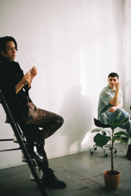 Free Two men posing in a minimalist studio setting with ladder and potted plant. Stock Photo