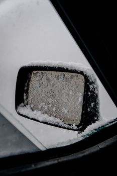 Close-up of a car side mirror with snow and ice in the winter season.