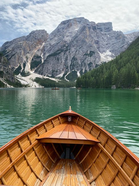 A wooden boat on calm waters against a backdrop of towering mountains and lush greenery.
