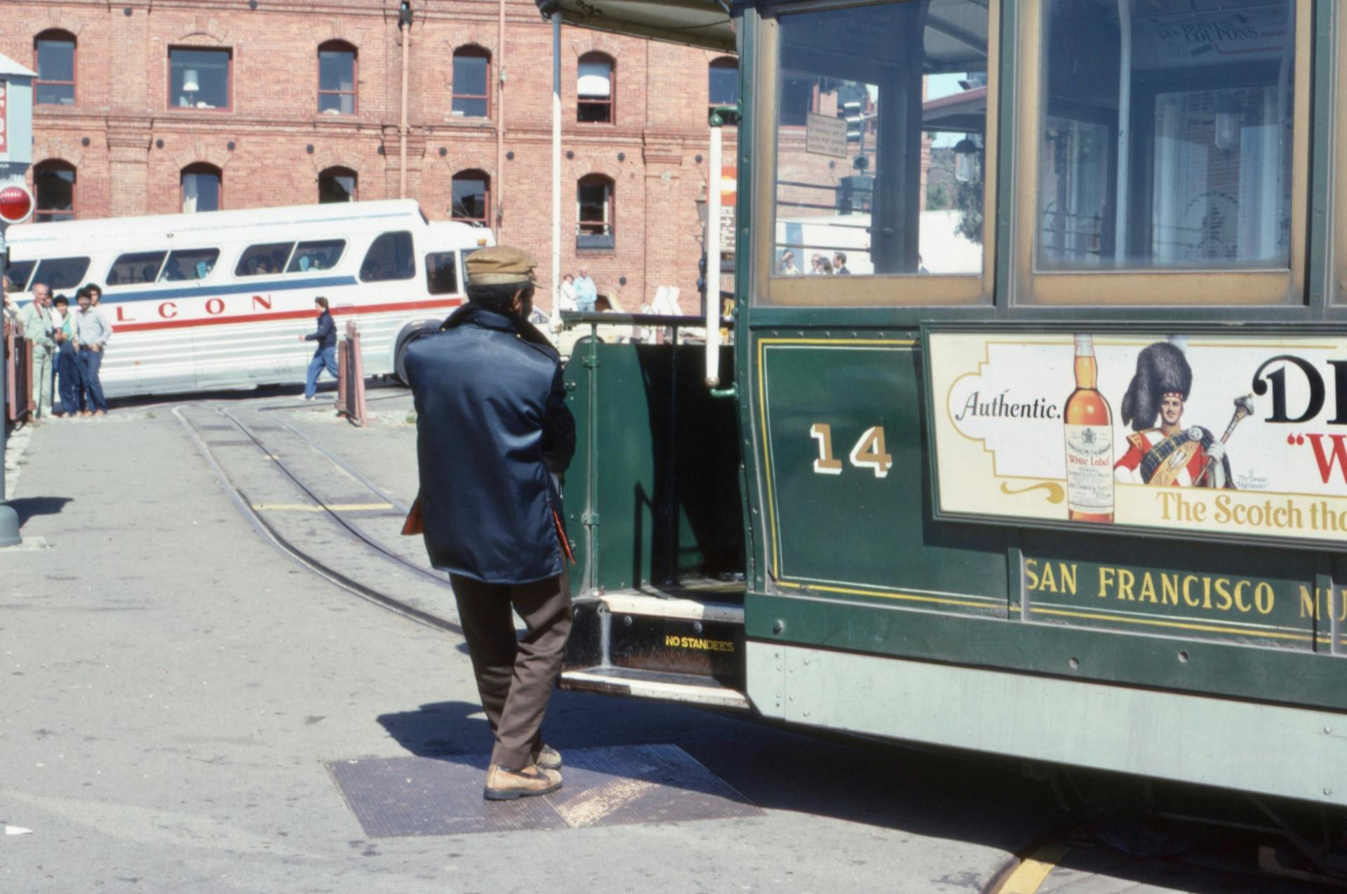 A man in a jacket boards a vintage tram in San Francisco on a sunny day.