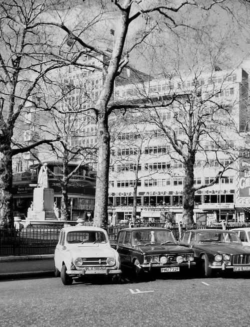 Free Black and white photo featuring vintage cars parked on a London street with buildings and trees visible. Stock Photo