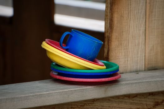 Vibrant colored plastic dishes and cup on wooden ledge, creating an artistic and playful scene.