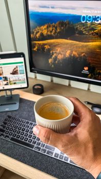 Hand holding coffee cup in front of computer screens, suggesting a tech-savvy workspace.