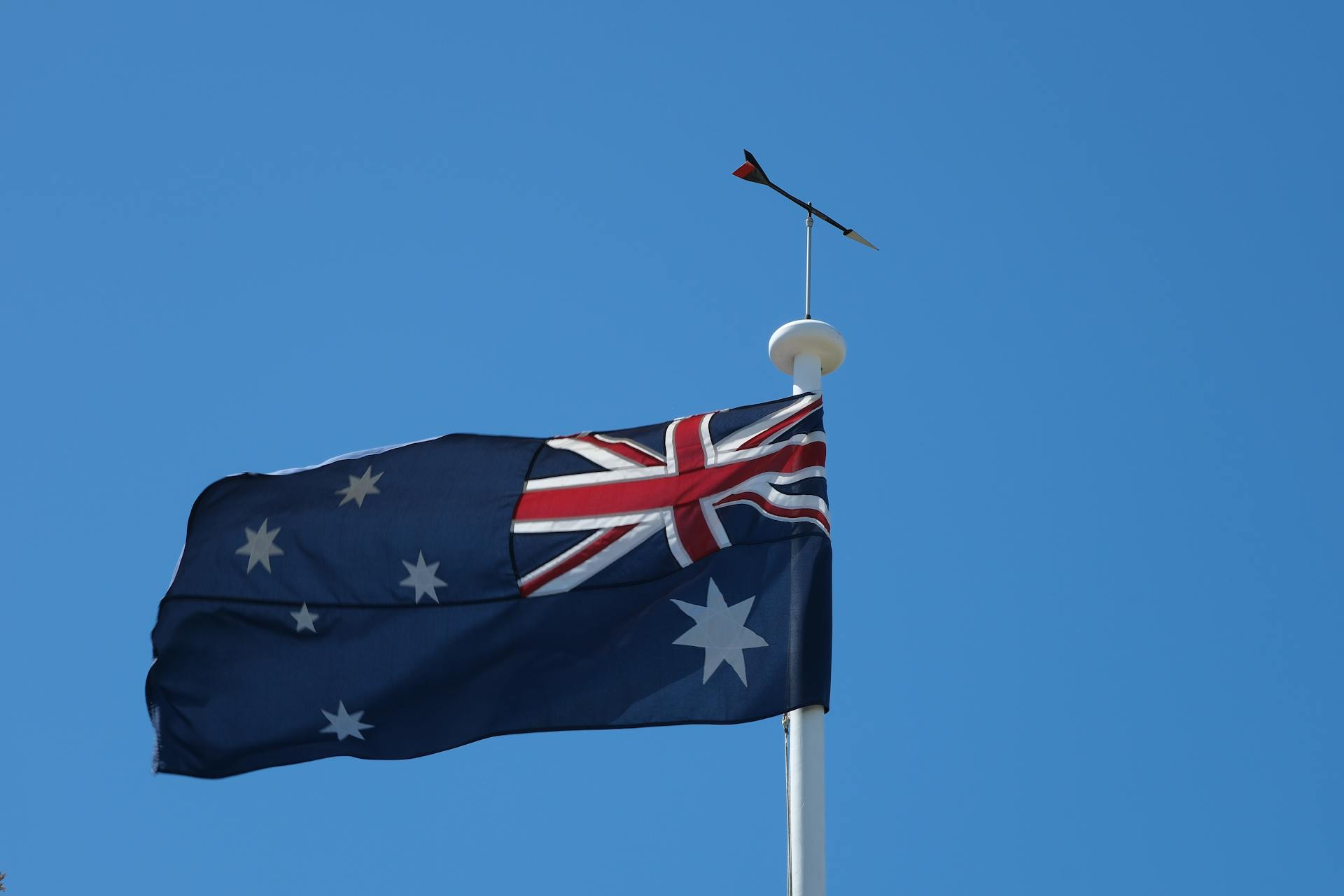 Close-up of the Australian flag on a flagpole waving against a clear blue sky.