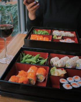 Sushi and edamame bento box meal served with wine at a restaurant. Perfect for lunch outings.