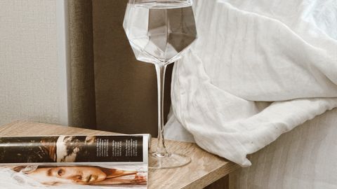 Stylish bedside table setup featuring a magazine and a geometric glass of water for a touch of elegance.