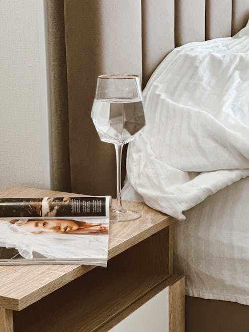 Free Magazine and Water in Wine Glass on Night Stand Stock Photo