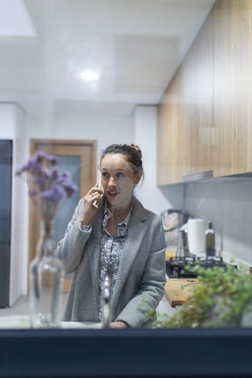 Mulher a falar ao telemóvel na cozinha à janela