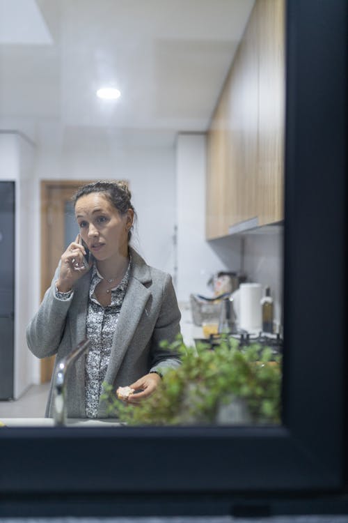 Mulher a falar ao telemóvel na cozinha à janela