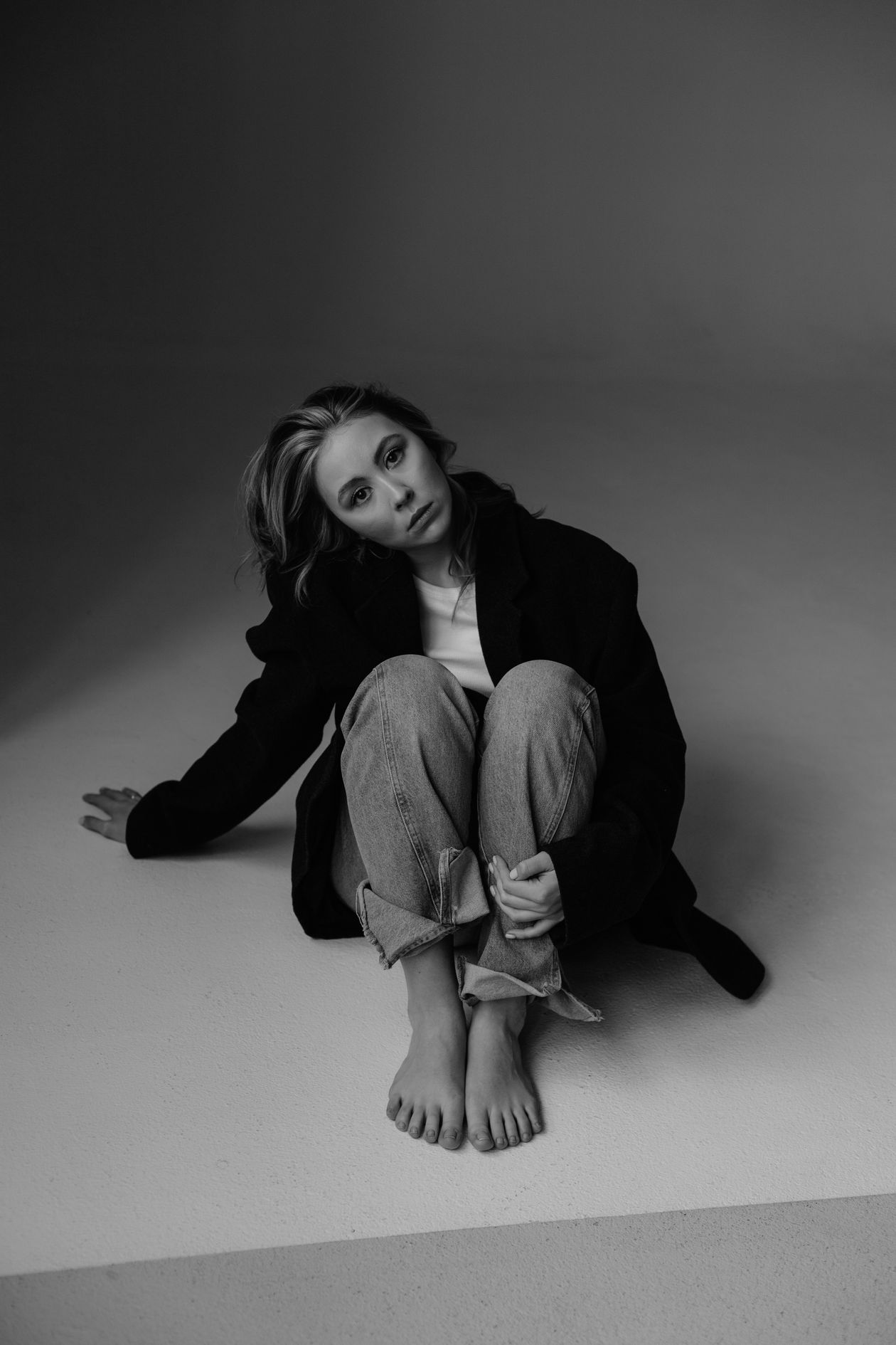 Woman in minimalist neutral outfit black coat white shirt sitting in studio portrait